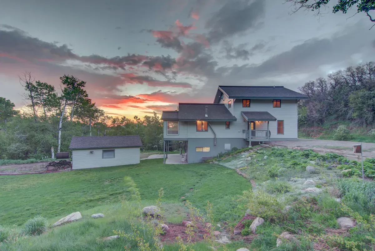 A large house is sitting on top of a hill with a sunset in the background.