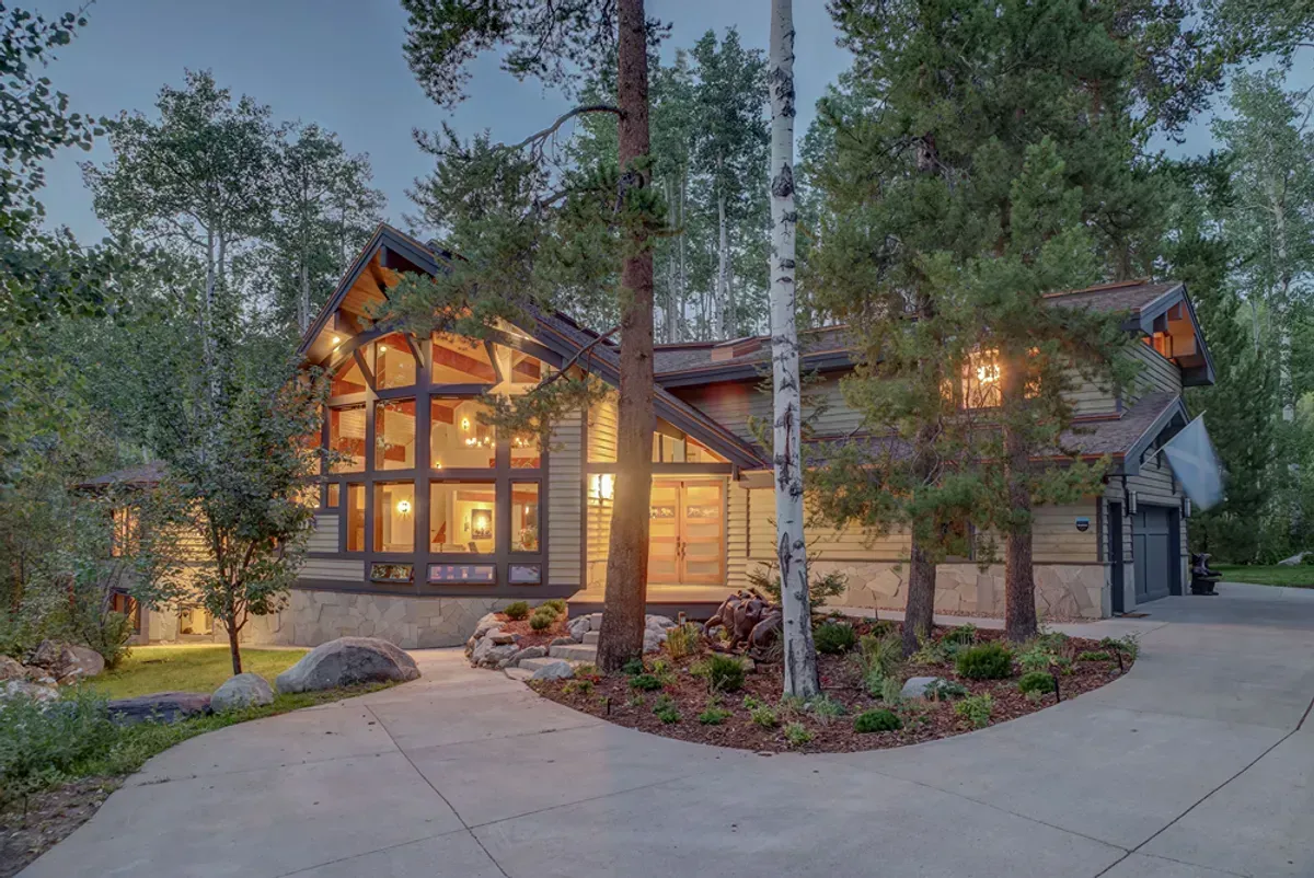A large house with a lot of windows is surrounded by trees and a driveway.