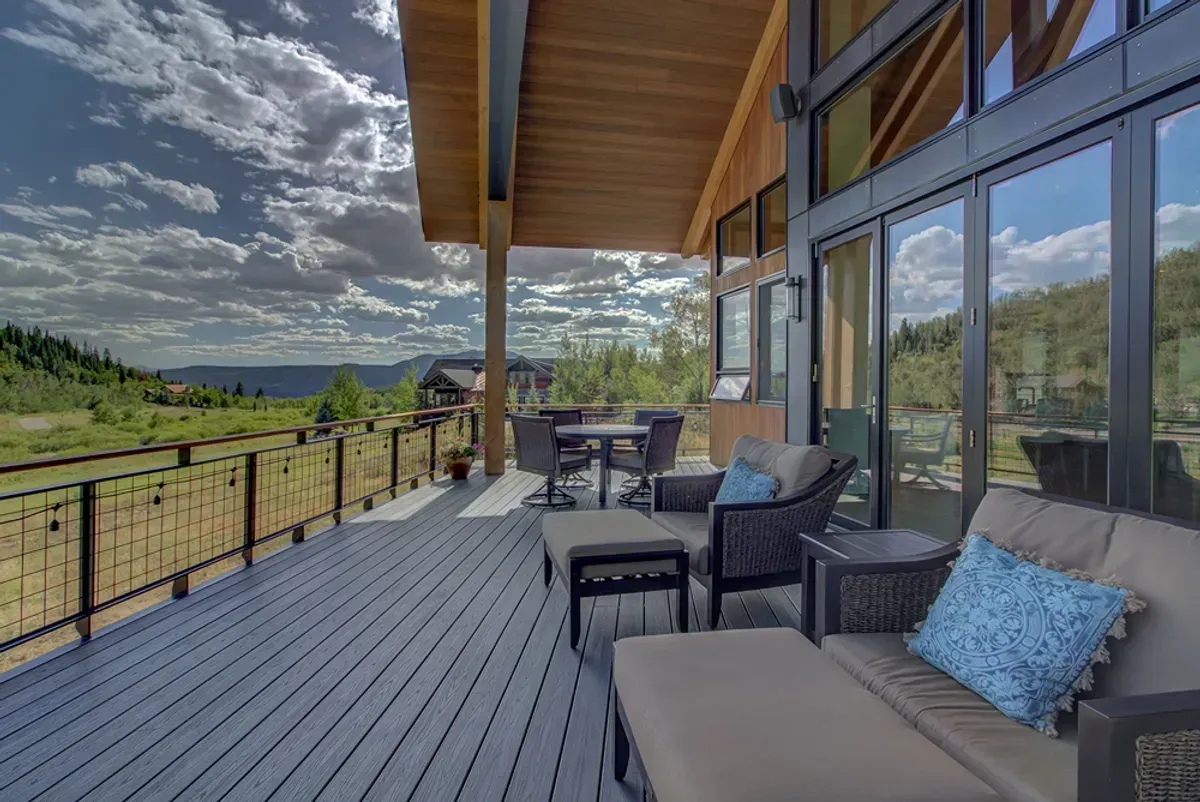 There is a large deck with a lot of windows and furniture on it.