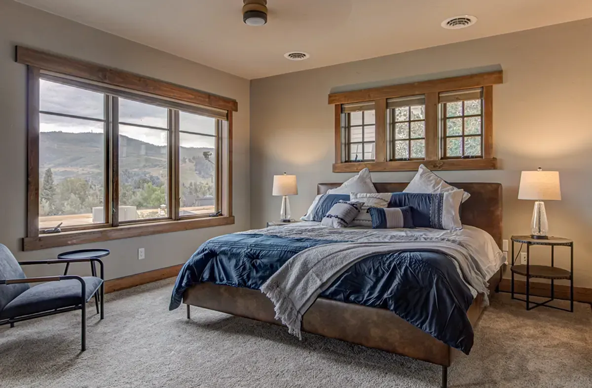 A bedroom with a king size bed , chairs , lamps , and windows.