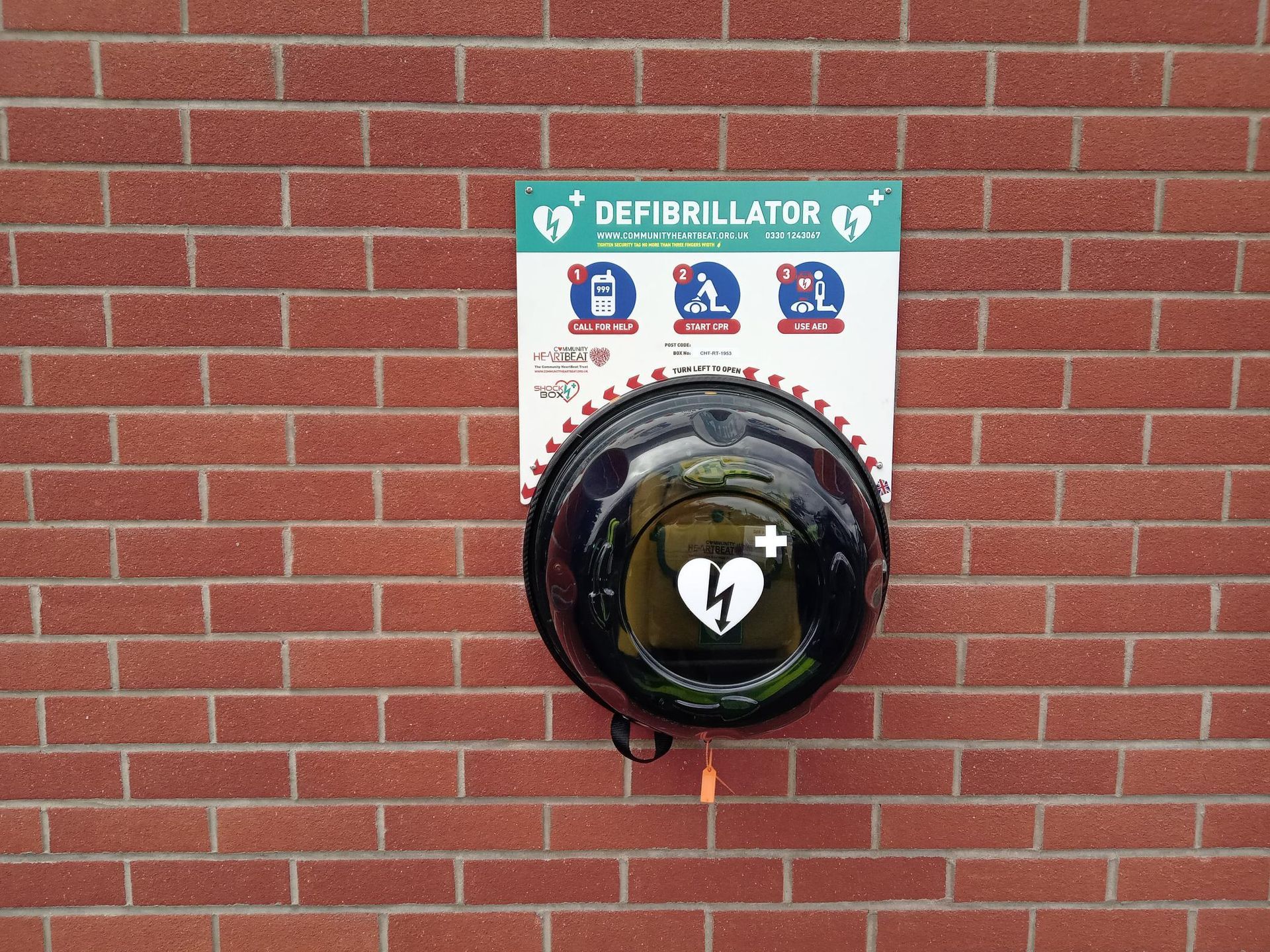 A defibrillator is mounted on a brick wall.