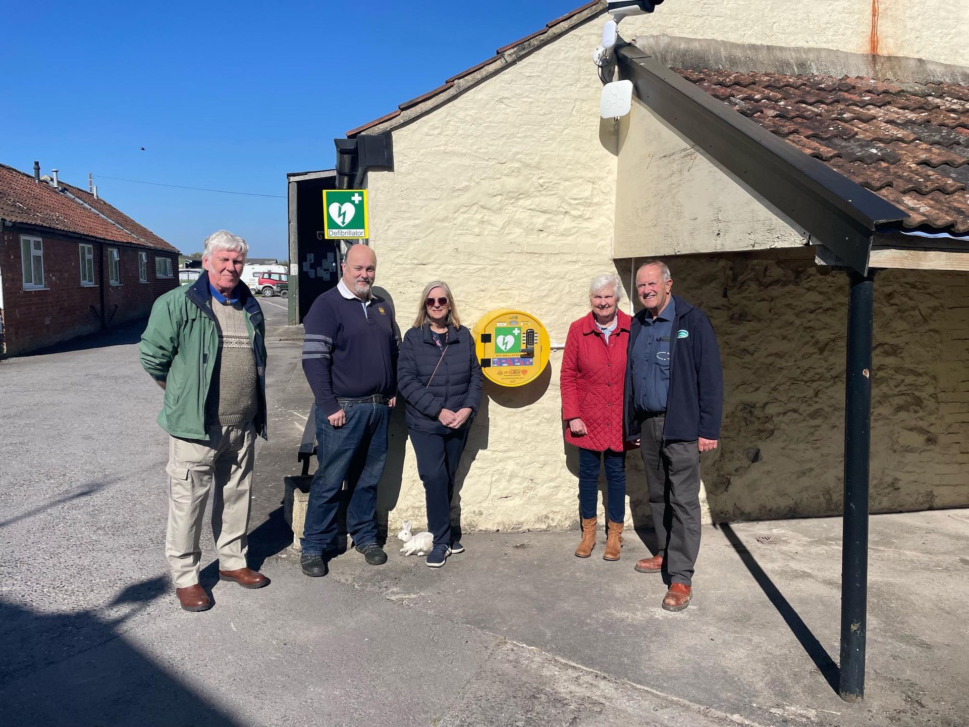 A group of people are standing in front of a building next to a defibrillator.