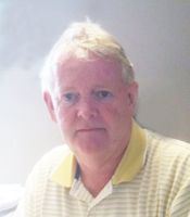 A man wearing a yellow and white striped shirt is looking at the camera.