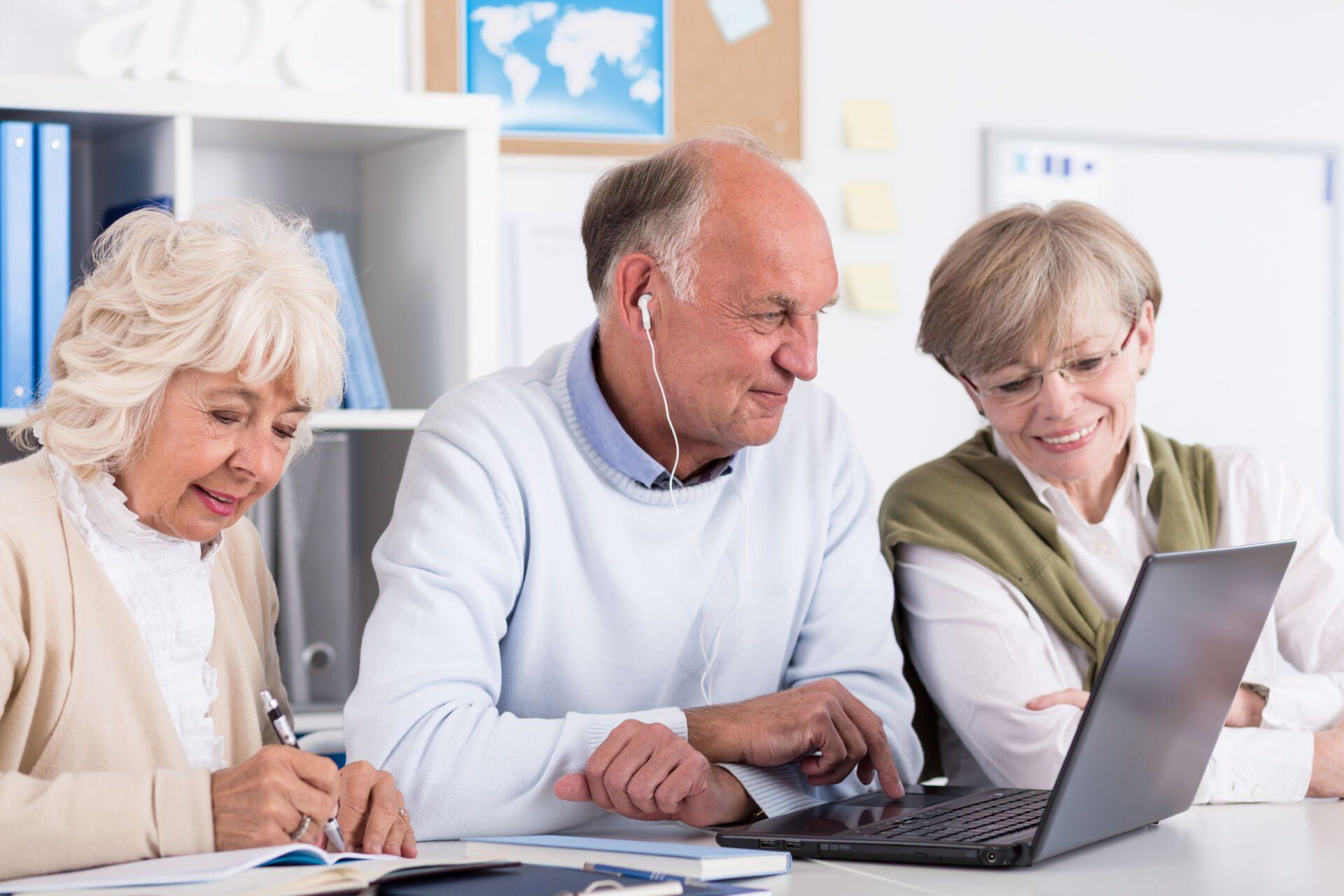 A group of elderly people are sitting at a table looking at a laptop computer.