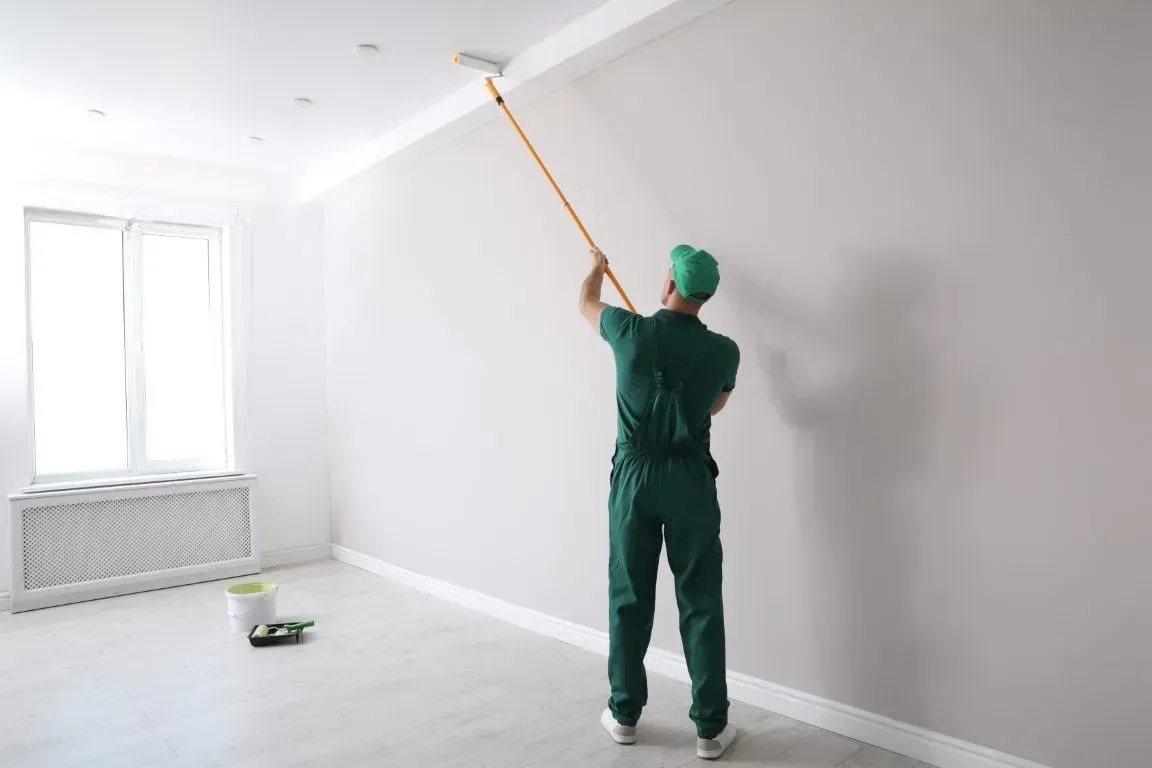 Interior painter using a roller extension pole on a white wall.