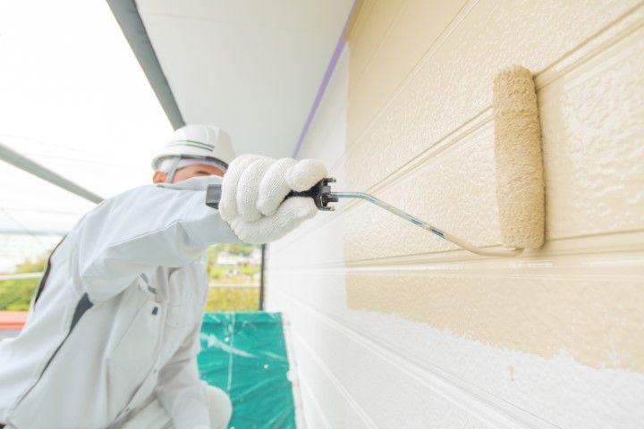 Exterior house painter applying beige paint to home siding.