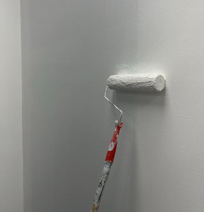 Paint roller applying white paint to a textured interior wall.