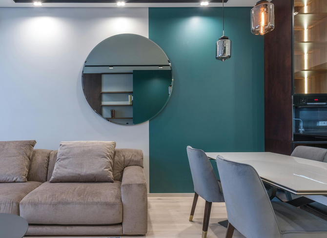 Modern living room with dark green accent wall and round mirror.