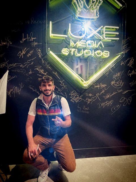 A man is kneeling in front of a sign that says luxe media studios