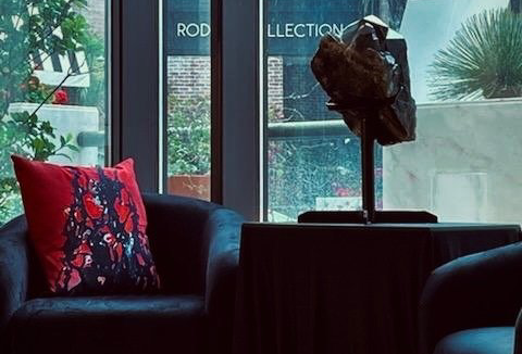 A chair with a red pillow sits in front of a window.