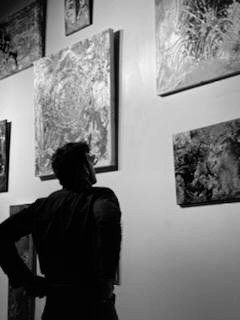 A man is looking at paintings on a wall in a black and white photo.