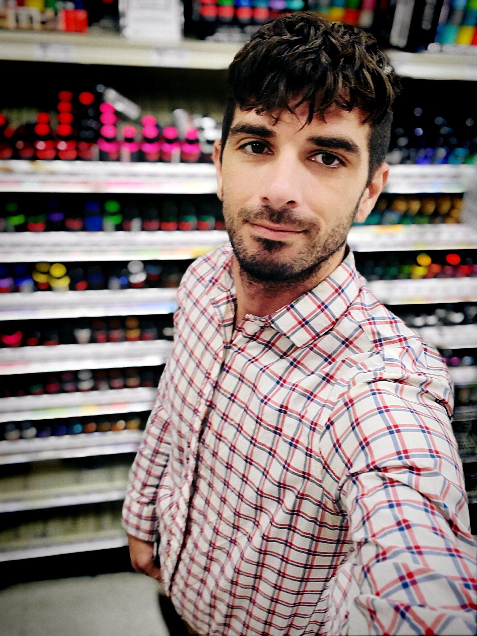 A man in a plaid shirt is taking a selfie in a store.