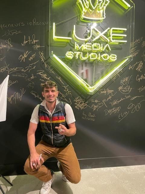 A man is kneeling in front of a sign that says luxe media studios.