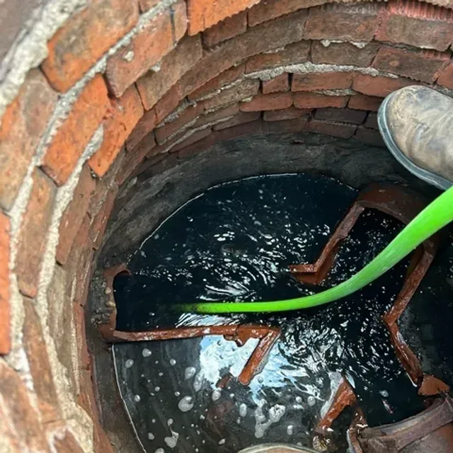 A person is pumping water into a well with a green hose