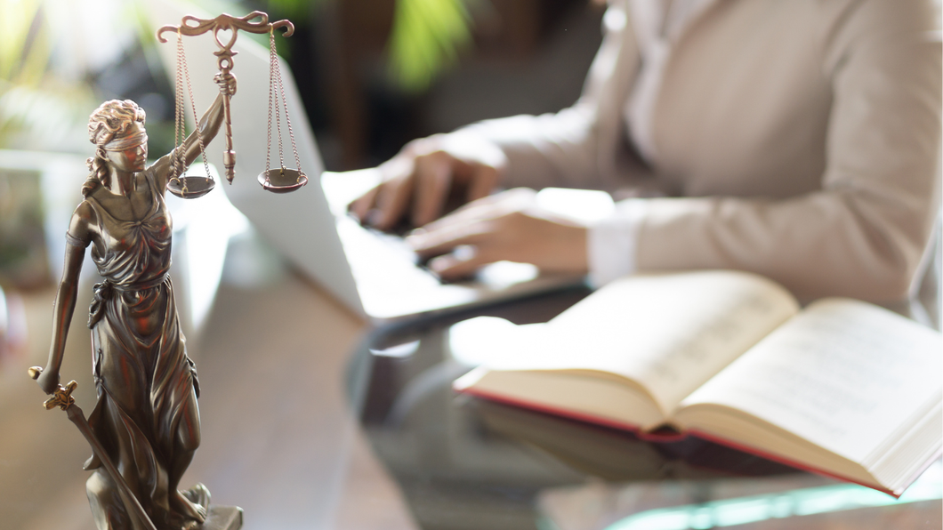 A statue of justice is sitting on a table next to a person using a laptop.