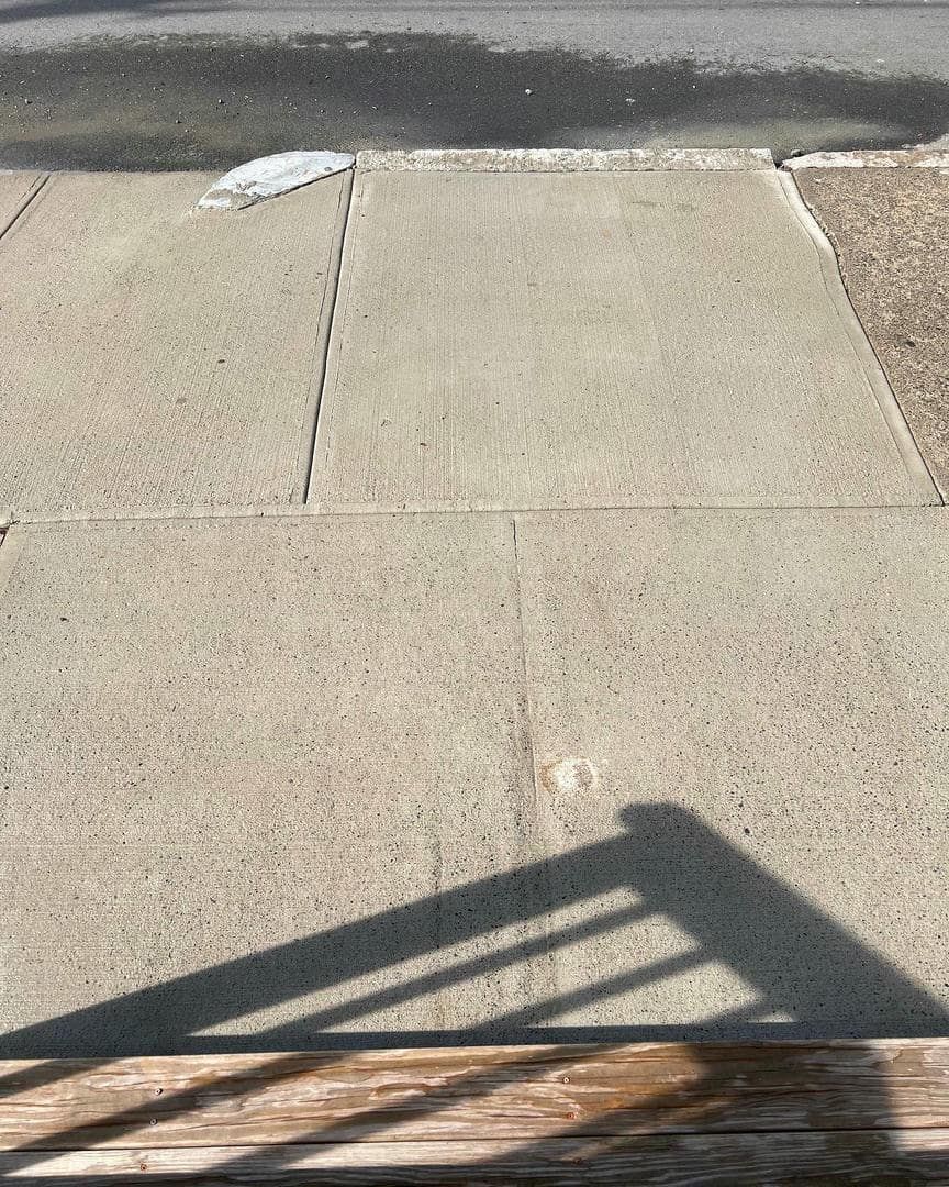 A shadow of a railing is cast on a concrete sidewalk.