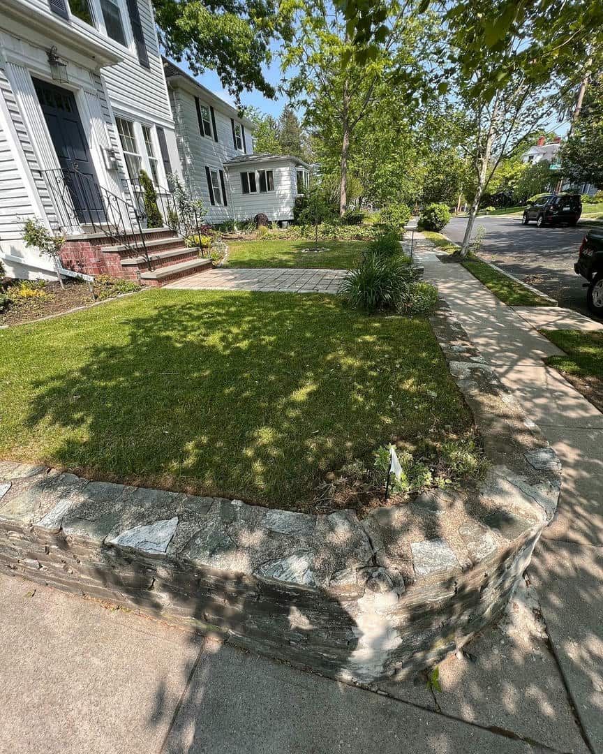 A sidewalk leading to a house with a stone wall in front of it.