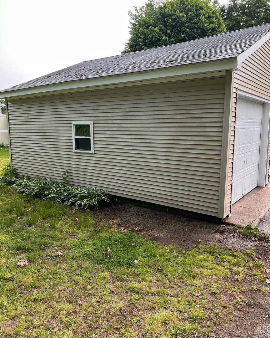 A garage with a window and a garage door is sitting in the grass.