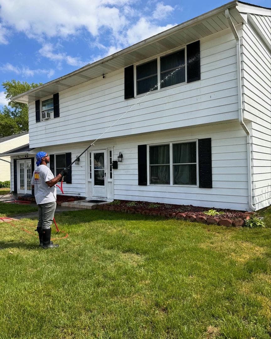 A man is cleaning the side of a white house with a pressure washer.
