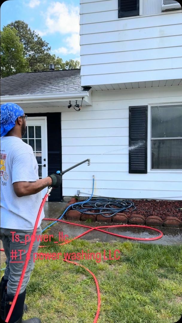 A man is cleaning the side of a house with a pressure washer.
