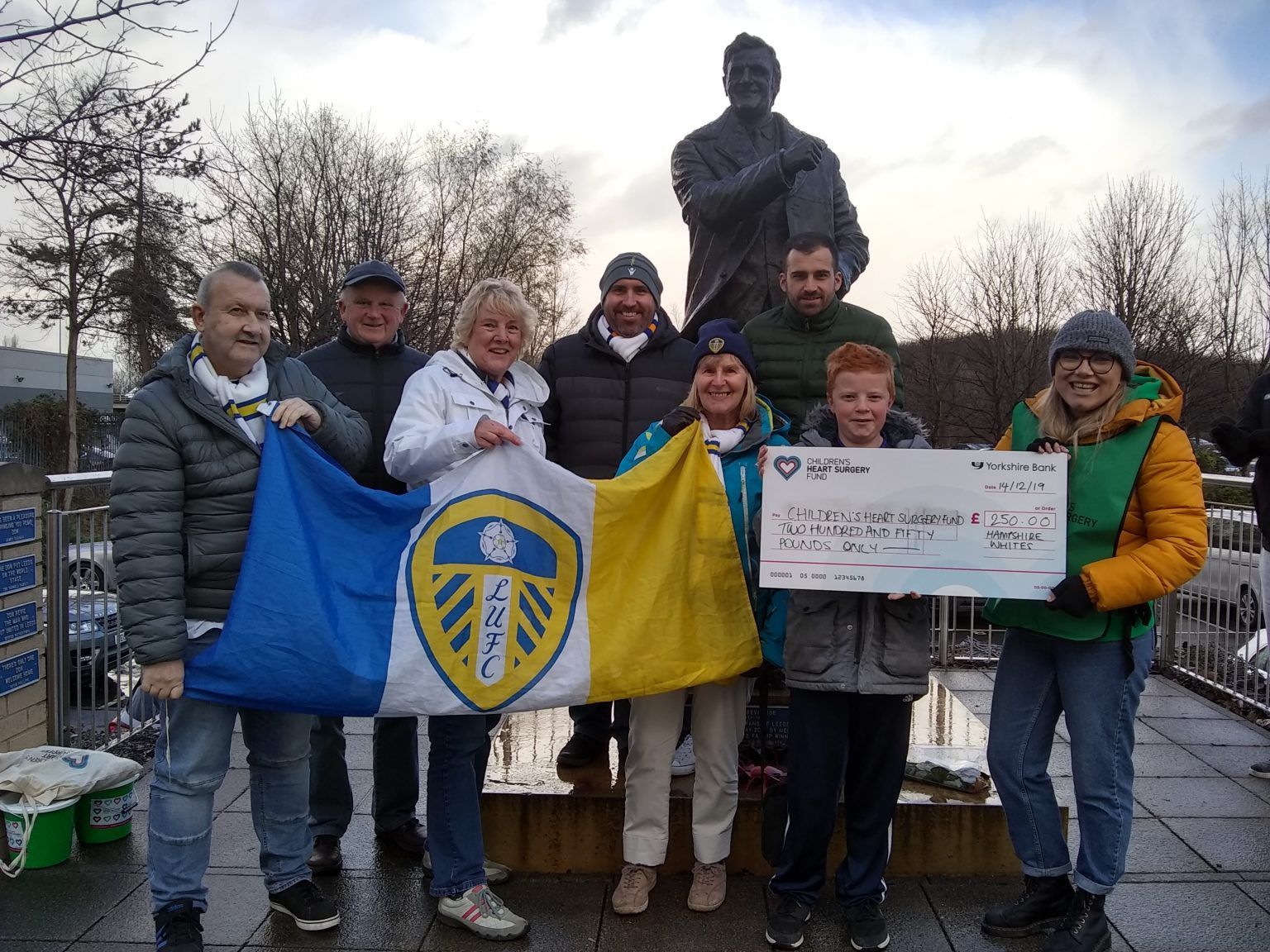 Hampshire Whites handing over cheque to a chosen charity in front of Don Revie statue