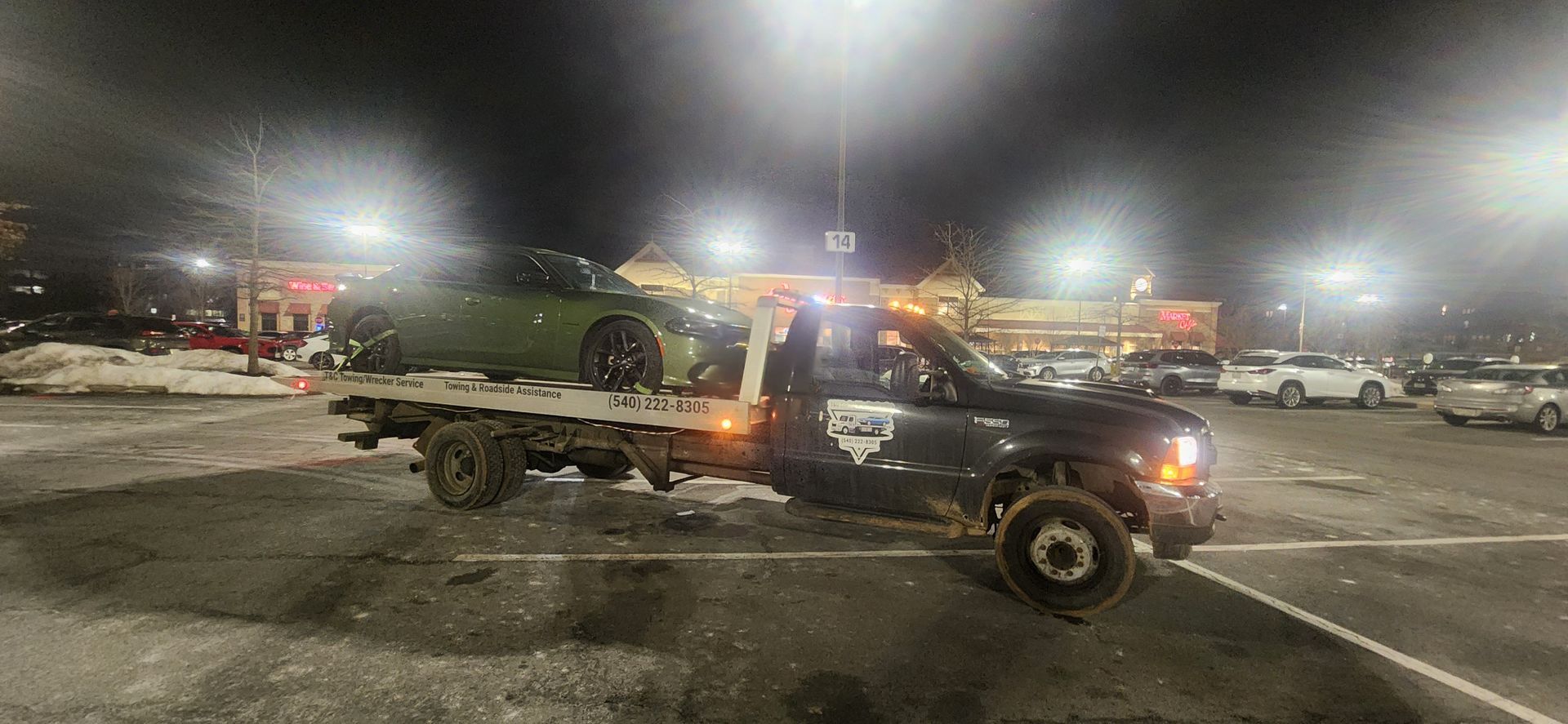 A tow truck is towing a car in a parking lot at night.