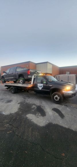 A tow truck is towing a pickup truck in a parking lot.