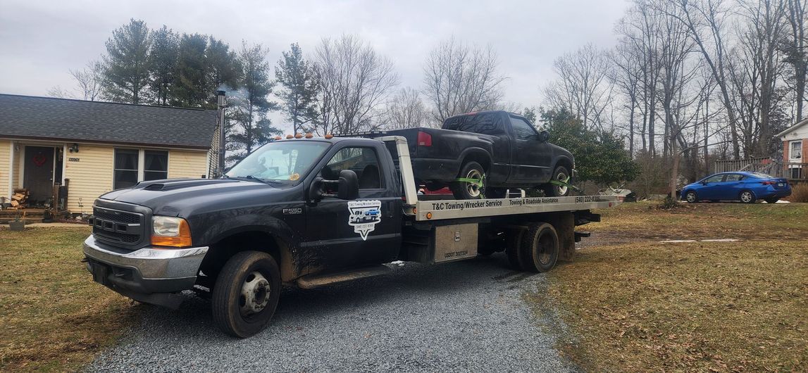 A tow truck with a car on the back is parked in front of a house.