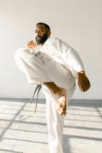 A man in a white karate uniform is kicking in the air.