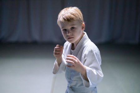 A young boy in a karate uniform is standing in a dark room.