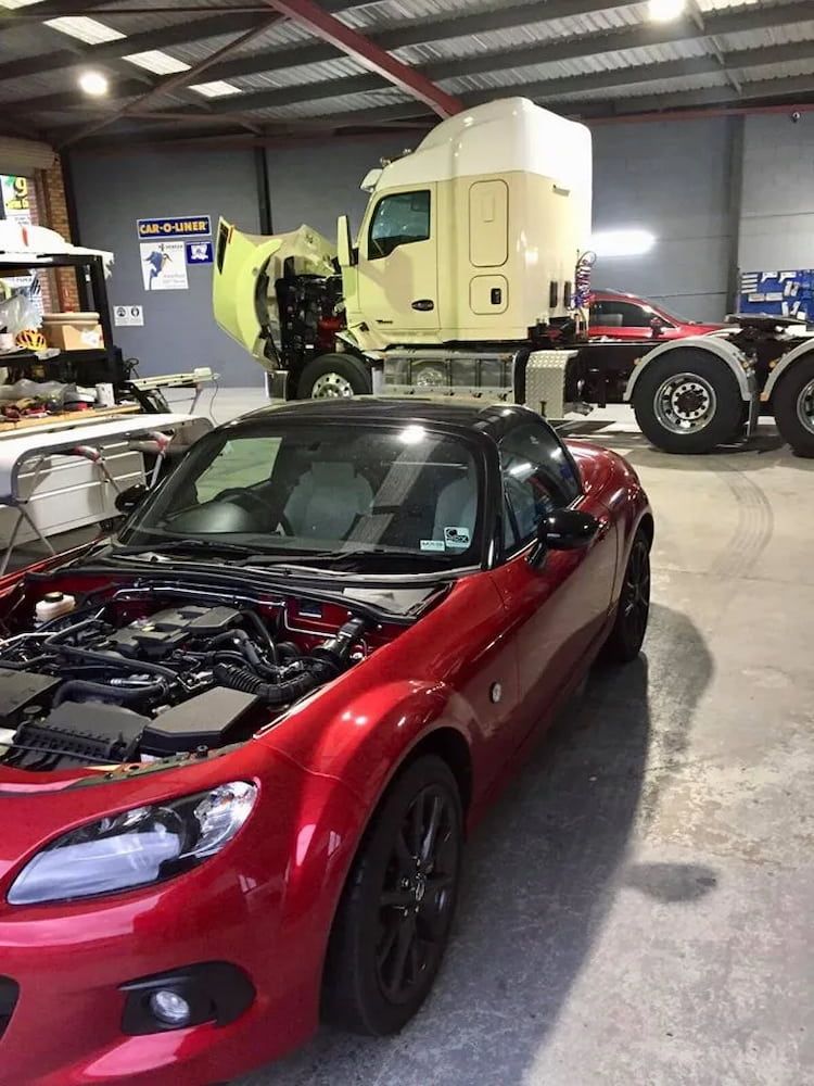 A Red Sports Car With the Hood Up is Parked in a Garage Next to a Semi Truck — Seabreeze Auto Body in Coffs Harbour, NSW