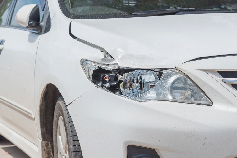 A White Car With a Damaged Headlight is Parked on the Side of the Road — Seabreeze Auto Body in Coffs Harbour, NSW