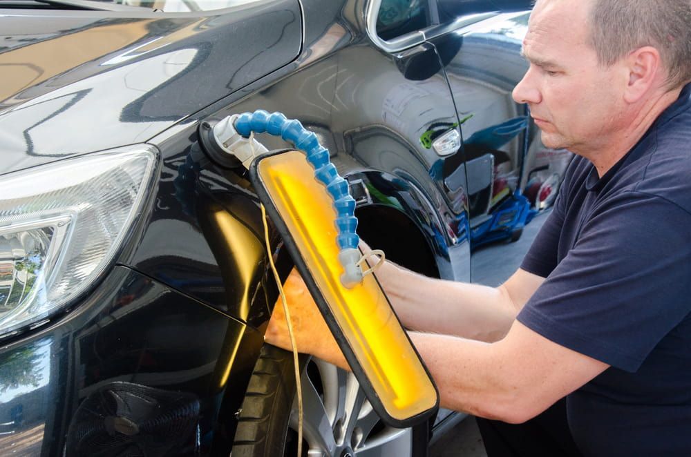 A Man is Working on a Car With a Yellow Light — Seabreeze Auto Body in Coffs Harbour, NSW