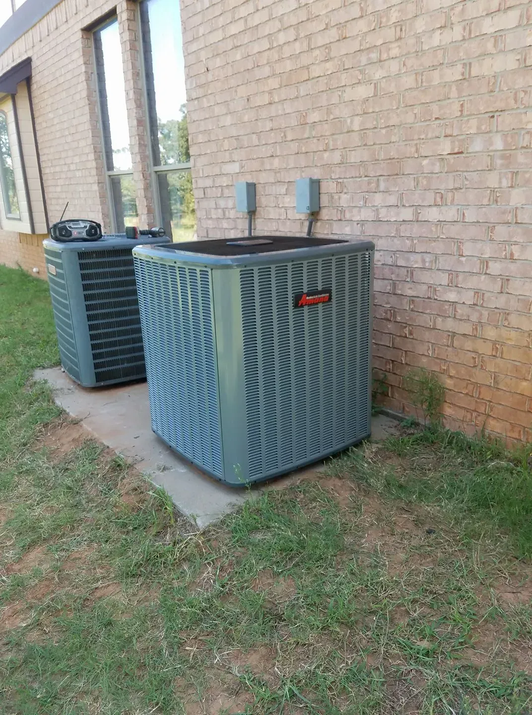 Two air conditioners are sitting on the side of a brick building.