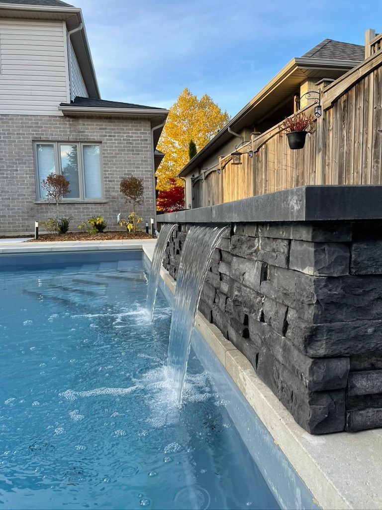 Pool with waterfall feature and stacked stone wall in a residential setting. Blue water and a sunny day.