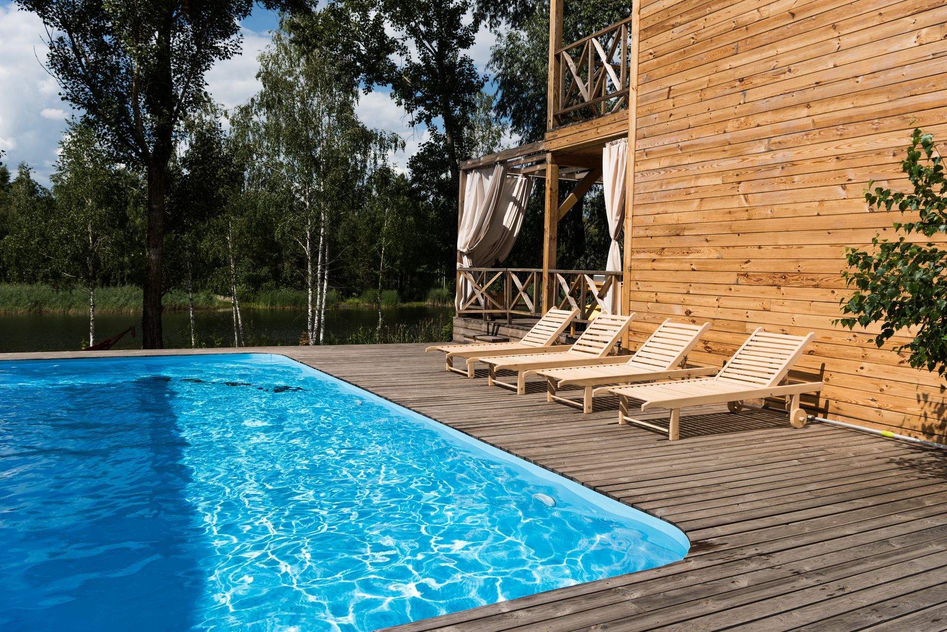 A large swimming pool is surrounded by chairs and a wooden deck.