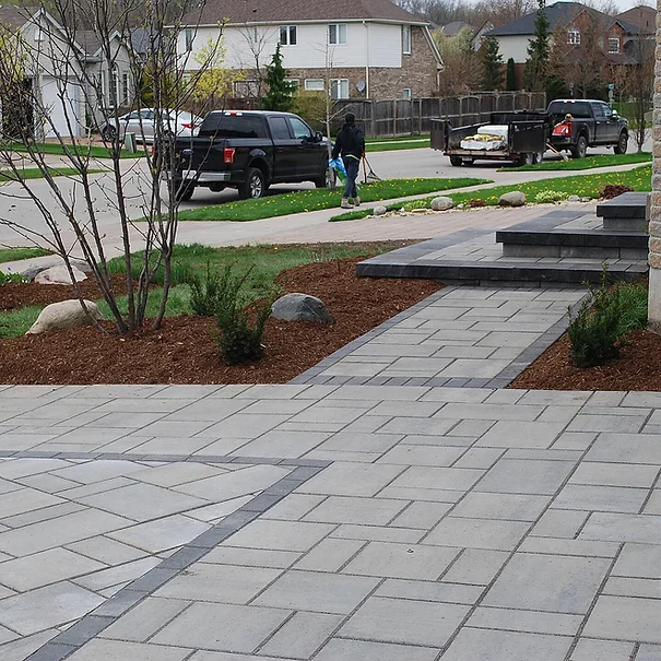 Brick walkway leading to a house with landscaping; person walks towards the vehicle.