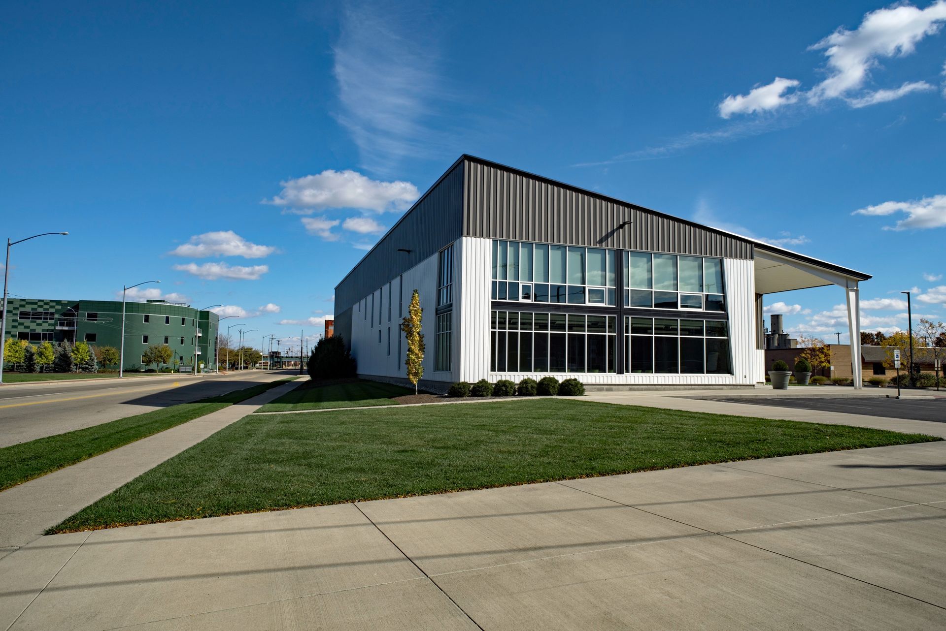 Modern building with a sloping gray roof, large windows, and a grassy lawn on a sunny day.