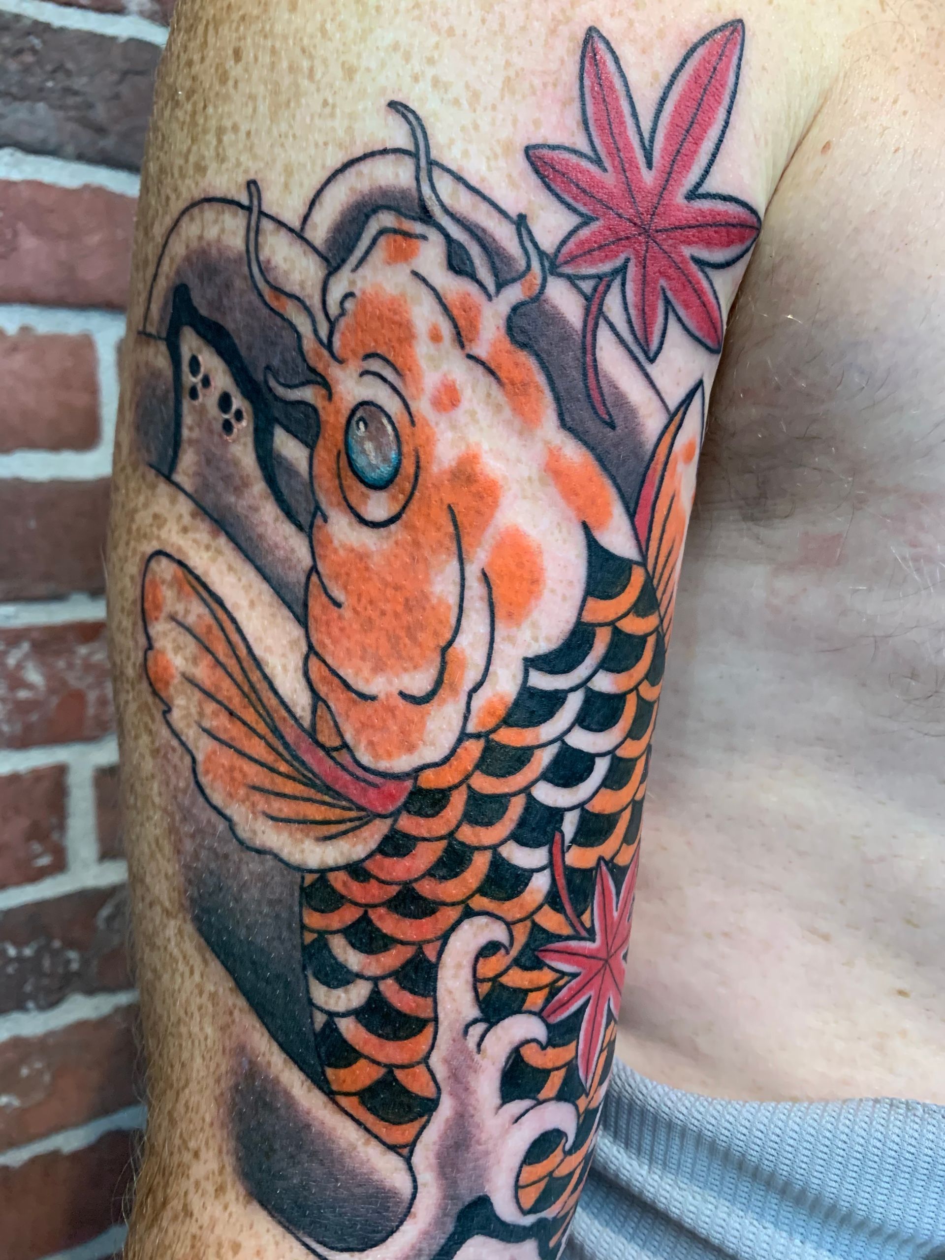 A man has a tattoo of a fish and a flower on his arm.