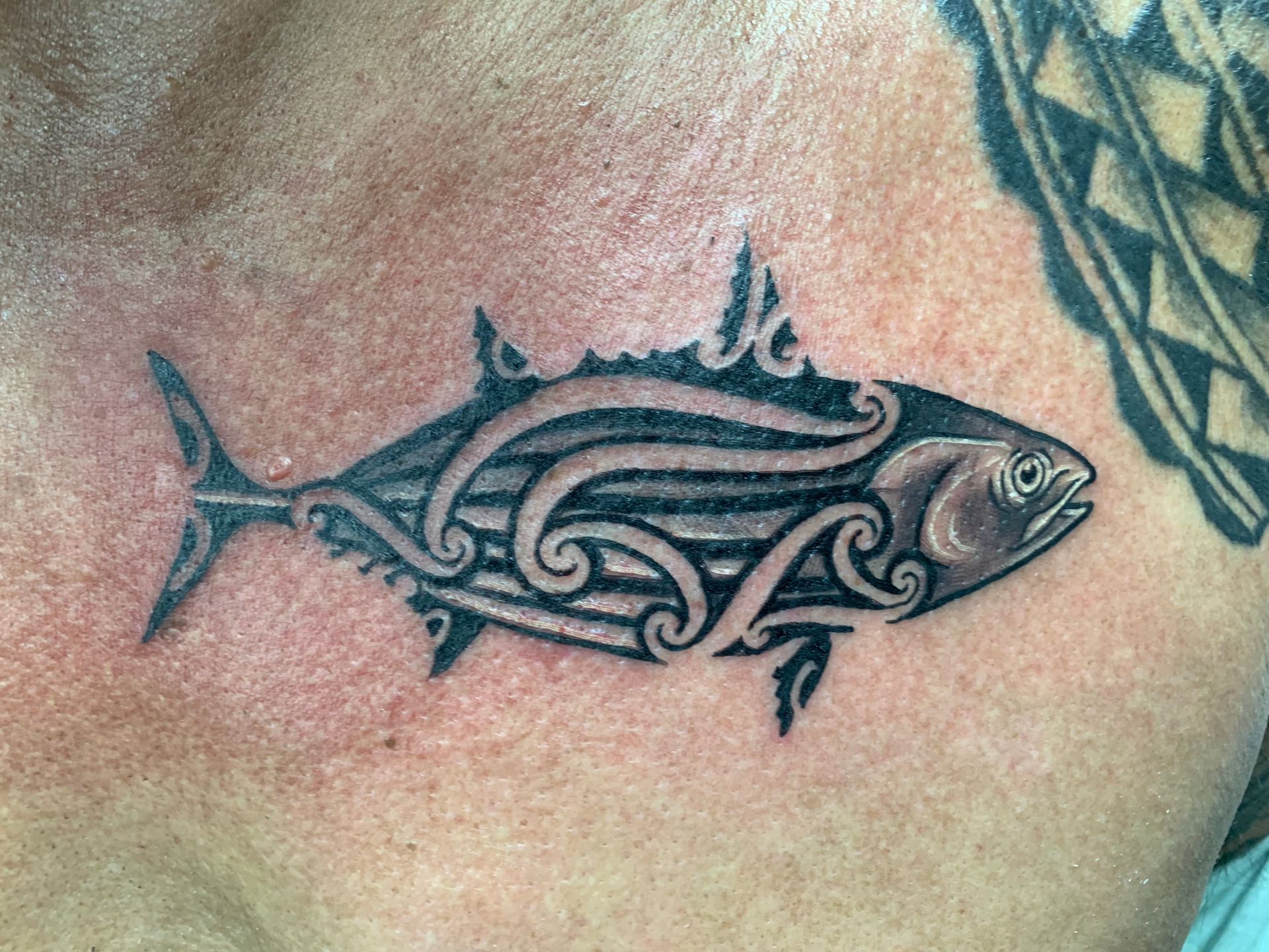 A man has a tattoo of a fish on his chest.