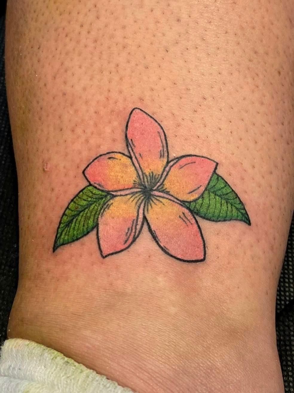 A person has a tattoo of a pink flower with green leaves on their leg.