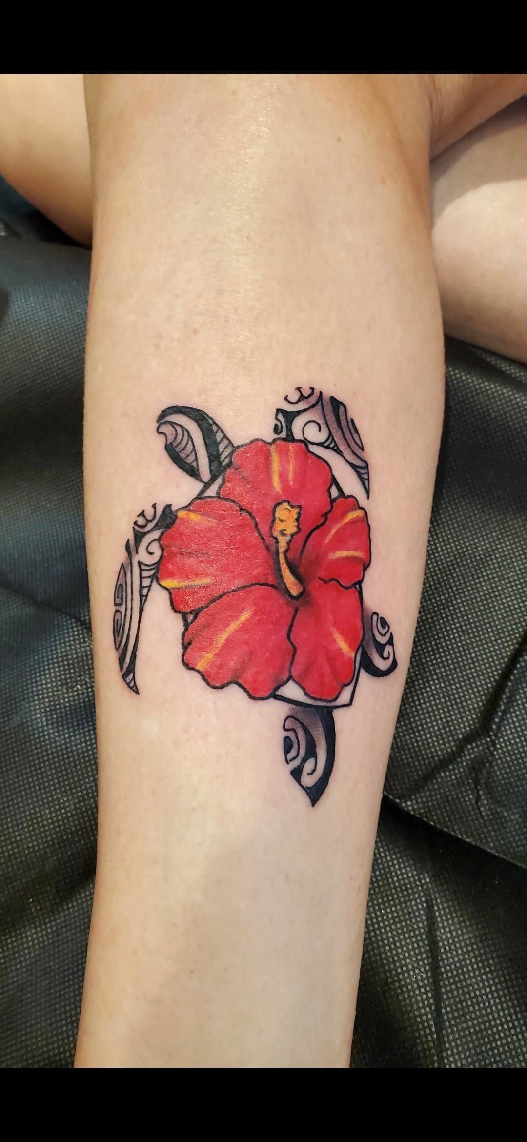A person has a tattoo of a turtle with a red flower on their arm.