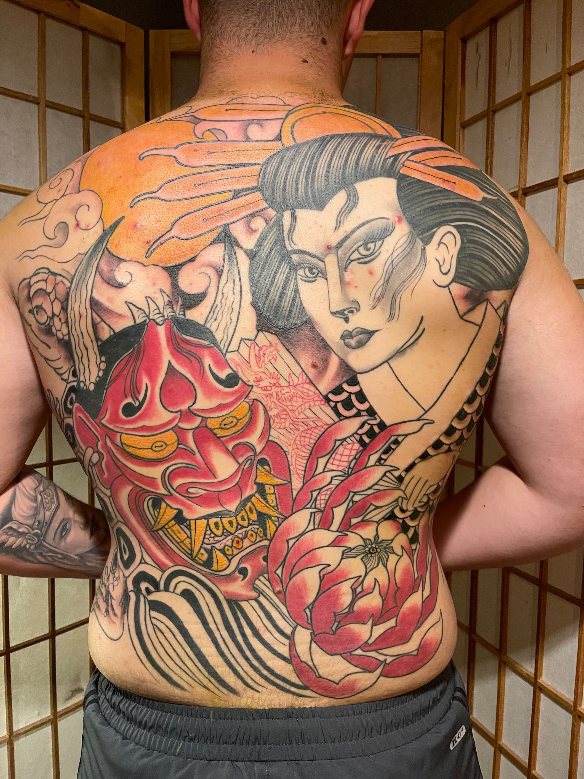 A man has a tattoo on his back of a woman and a demon.