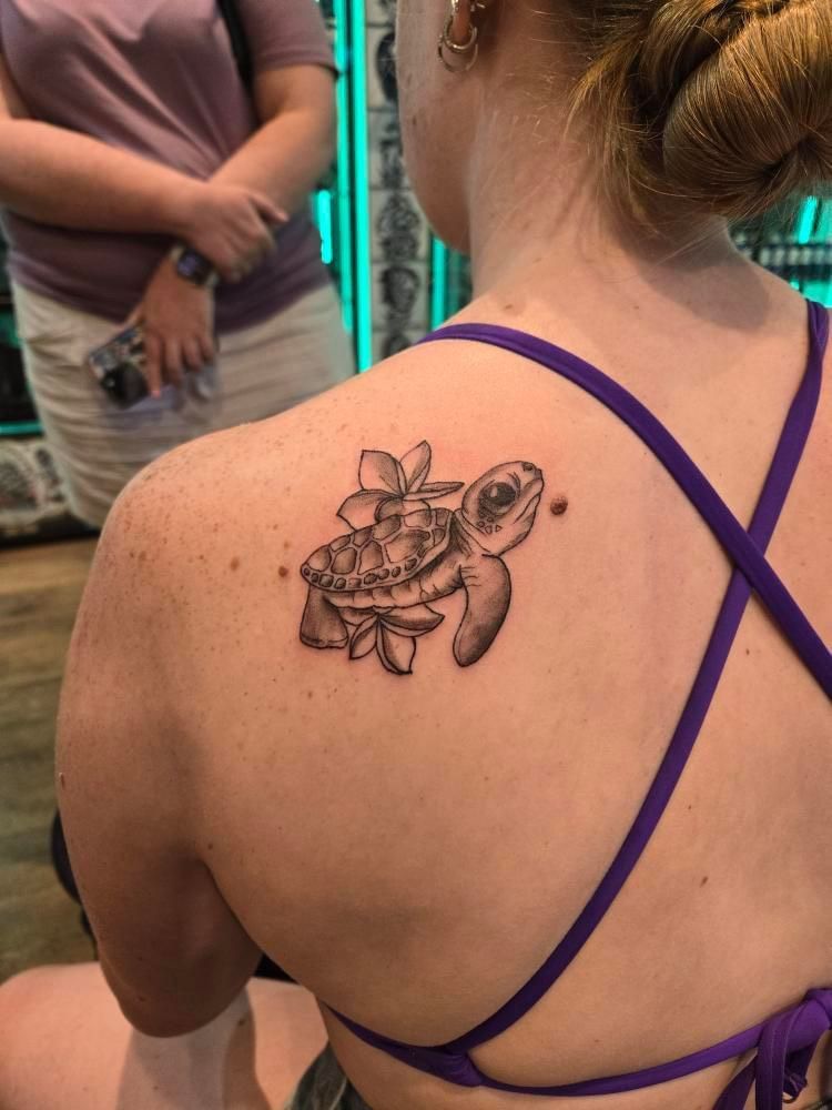 A woman has a tattoo of a sea turtle on her back.