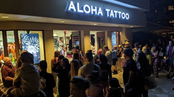 A large group of people are standing outside of aloha tattoo.