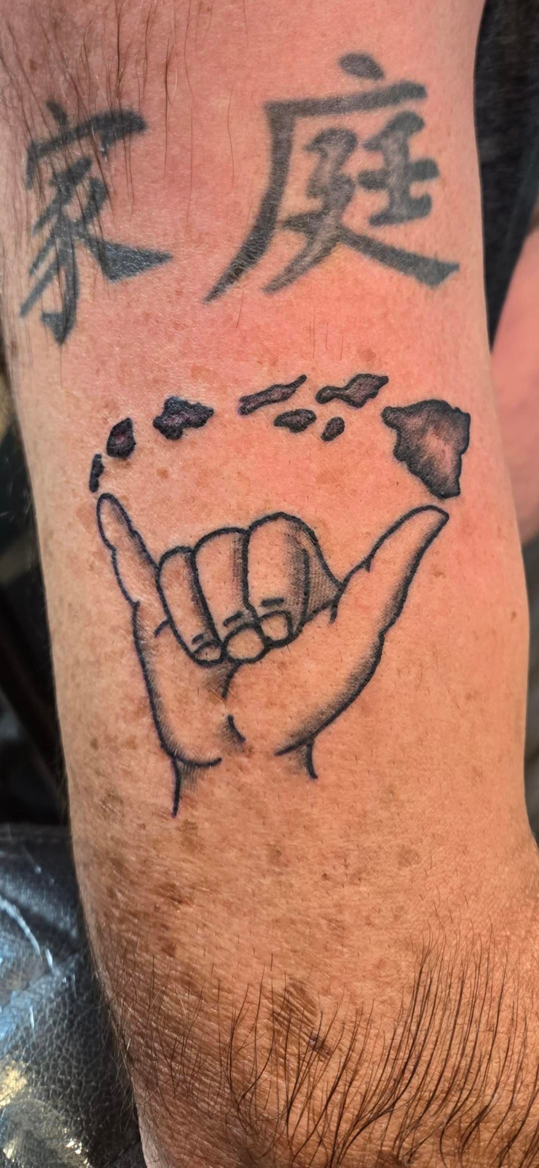 A man has a tattoo of a hand making a hang loose sign on his arm.