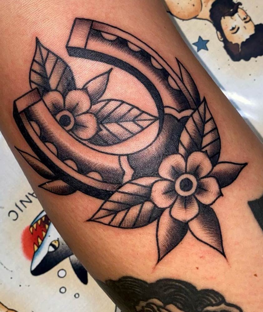 A tattoo of a horseshoe with flowers and leaves