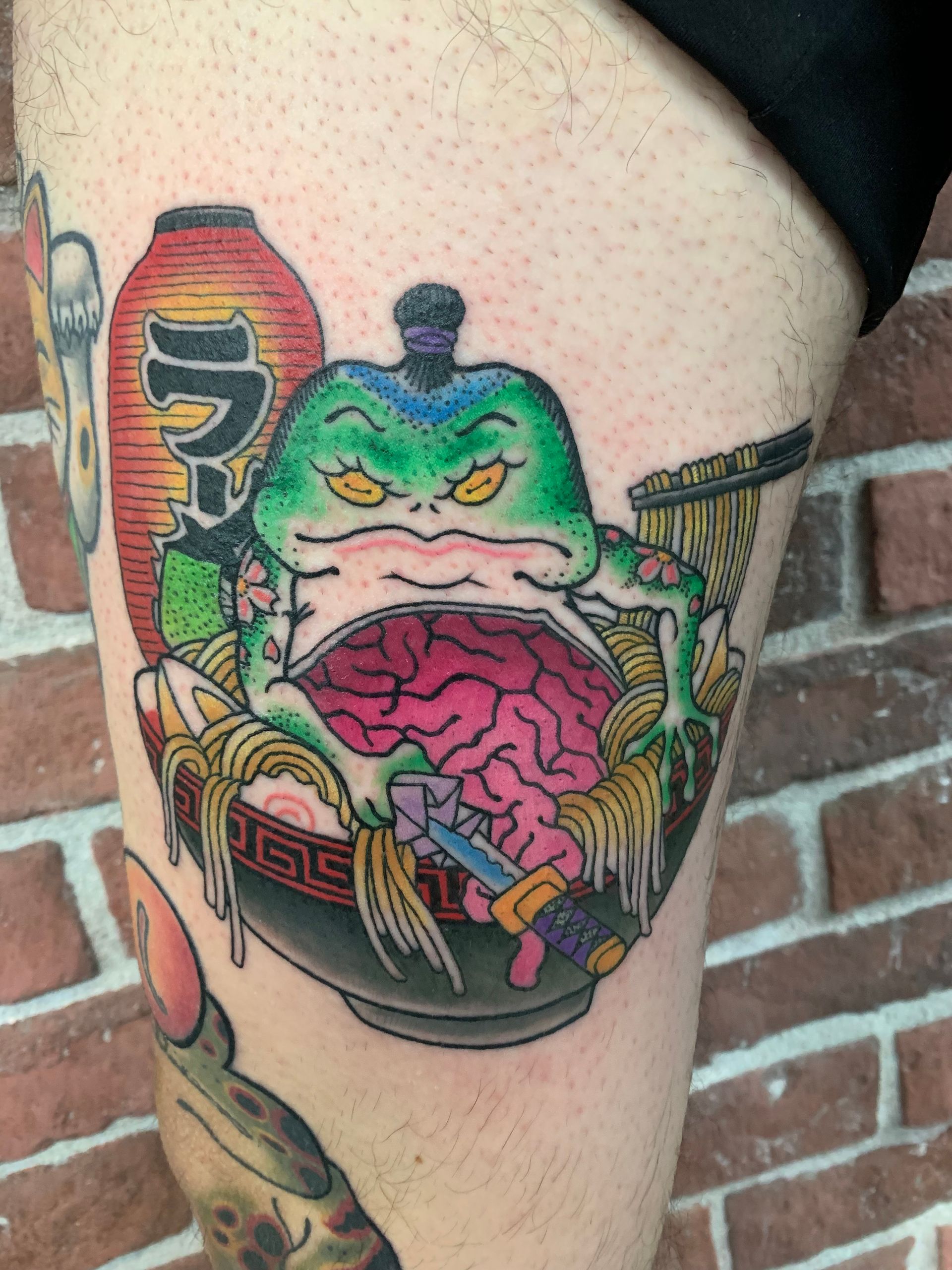 A person has a tattoo of a frog in a bowl of ramen