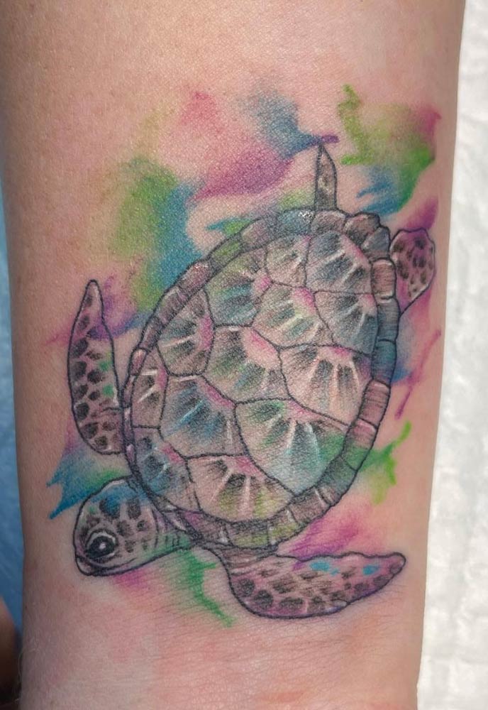 A watercolor tattoo of a sea turtle on a person 's arm.