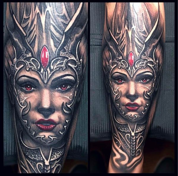 A tattoo of a woman with red eyes and a crown on her head.